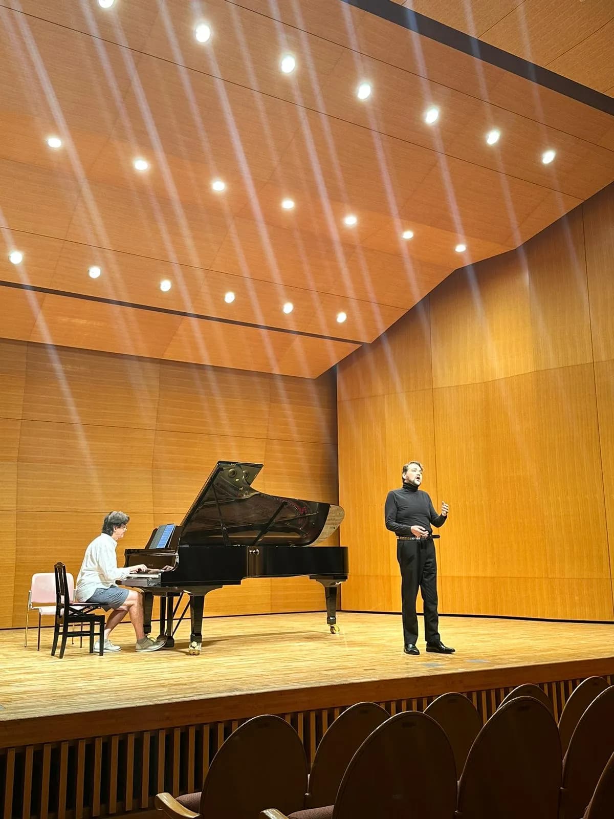 Ebro mid-phrase on the recital stage, pianist and hall in frame